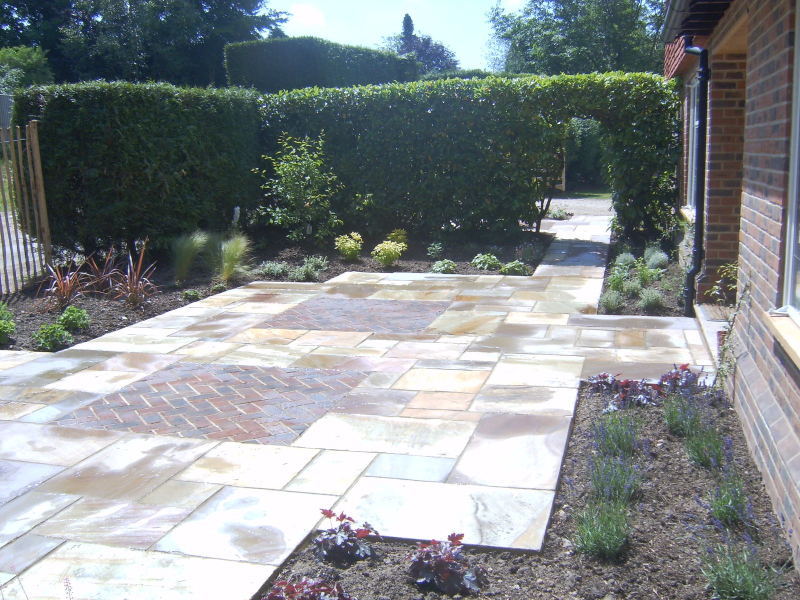 Indian sandstone paving with brick infills and pergola in a Grayshott garden